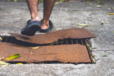 Yaya ayakları sandalet giyer hasarlı kanalizasyon borularının üzerinde yürür ve paslı çelik plakalarla kaplıdır. Rögar kapağı kırılmış. Yoldaki çukur. Paslı rögar kapağı. Şehirdeki kanalizasyon kapağındaki kaza..