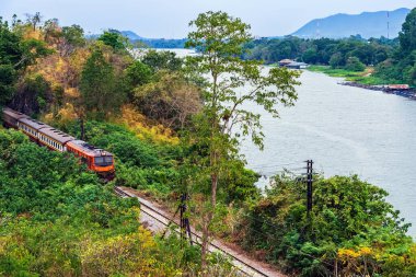 Kwai nehri boyunca tren yolculuğu. Trenin Tham Khao Pun Tapınağı 'ndaki yeşil tepelerle çevrili ünlü tren yolu kavşağının manzarası. 2. Dünya Savaşı Demiryolu, Tayland.