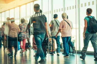 Kalkan yolcuların ve arka plandaki terminalden uçağa yürüyen bagajların bulanık görüntüleriyle dolu geniş cam duvarın içinden fotoğraf çekin. Cam üzerine seçici odaklanma.