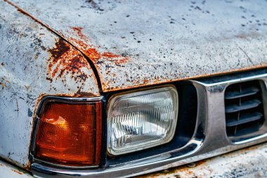 Tampon ve kaputta hasar görmüş eski paslı beyaz araba. Araç kaputunun üstünde paslanmış, çatlamış ve kabuğu soyulmuş. Araba vucudunda bozulma ve pas. Paslı bir kaput parçası..