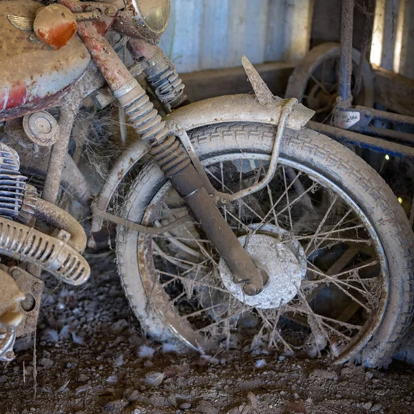 Closeup of the front wheel of a rusted vintage motorcycle covered in dirt and cobwebs