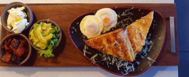 Kahvaltı tabağı olarak Türk tostu, haşlanmış yumurta, avokado, fırında domates ve yoğurt servis ediliyor.