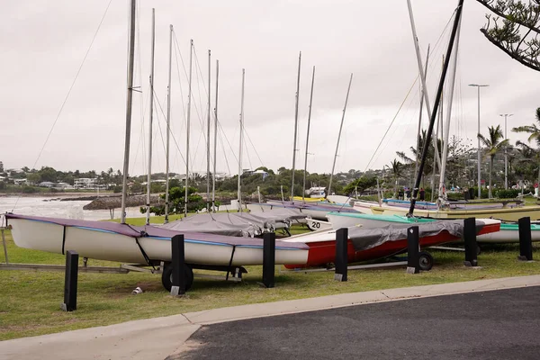 Small sailing yachts parked on their trailers on a grassy patch by the ocean on a rainy overcast day
