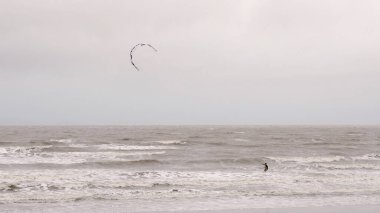 Yeppoon, Queensland, Avustralya - Nisan 2021: Yağmurlu ve rüzgarlı bir günde dalgalarla savaşan yalnız bir rüzgar sörfçüsü