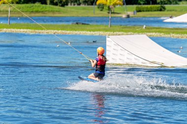 Mackay, Queensland, Avustralya - Nisan 2021: Emniyet kaskı ve can yeleği takan genç bir kız bir kablo parkında dizlerinin üzerinde geziniyor.