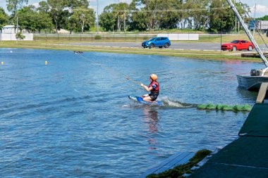 Mackay, Queensland, Avustralya - Nisan 2021: Emniyet kaskı ve can yeleği takan genç bir kız bir kablo parkında dizlerinin üzerinde geziniyor.