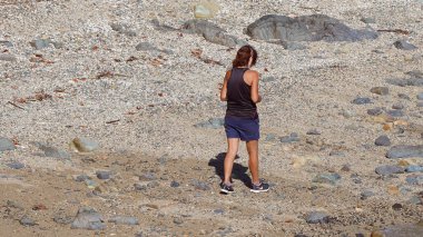 Airlie Beach, Queensland, Avustralya - Nisan 2021 Taşlı bir plajda yürürken kulak tıkaçları takılı genç bir kadın müzik dinliyor