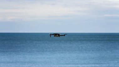 Drone hovering over water just below the horizon ready to take off and photograph the ocean and landscape
