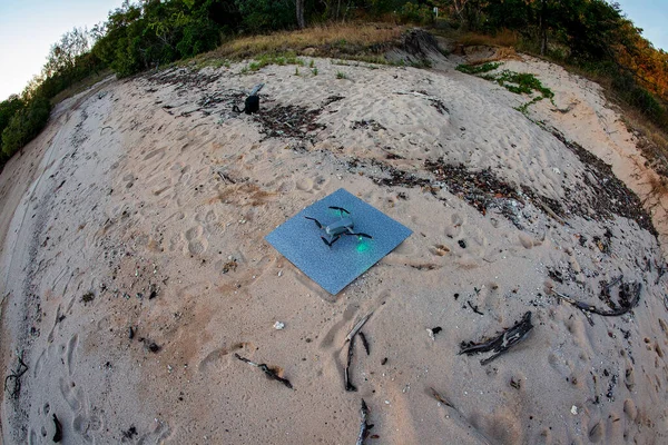 A drone on its landing pad on the sand on a secluded beach after photographing the sunrise, fish eye lens