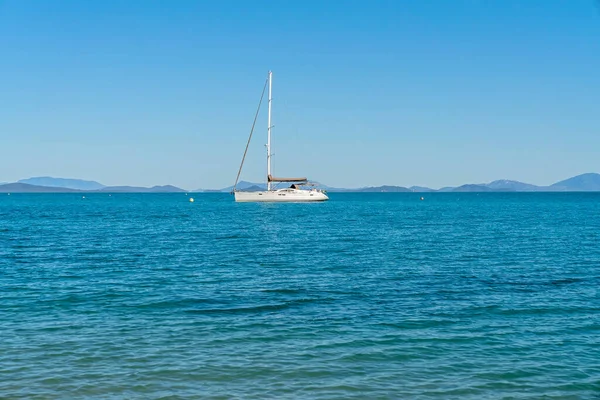 一艘豪华游艇 船桅下垂 停泊在海岸外的一个海湾里 海水清澈 天空蔚蓝 — 图库照片