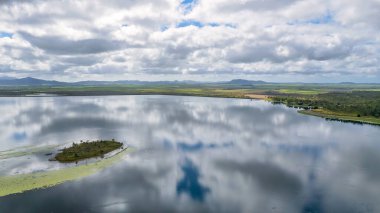 Bulutlar aynaya yansıyor baraj suyunun yüzeyi gibi minicik bir adadan kıyıya doğru. Kinchant Barajı, Queensland, Avustralya.