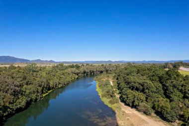 Bulutsuz mavi gökyüzünün altında kıyıları kaplayan çalılık bir derenin insansız hava aracı antenleri.