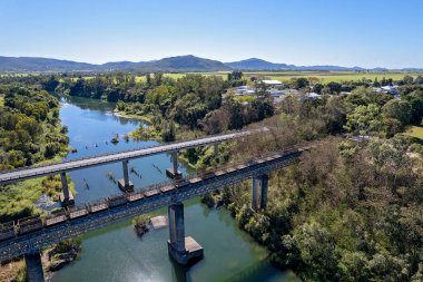 Boş şeker kamışı kutularının havası bir köy deresi boyunca bir otoyol köprüsüne paralel bir tren tarafından çekiliyor.