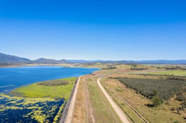 Aerial view along a dam wall showing a small green island of land on the edge of the water