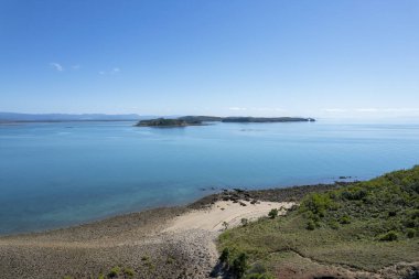 Kayalık bir adanın üzerindeki hava dalgaları kumlu sahil ve okyanus manzarası boyunca yürüyen yolları gösteriyor.