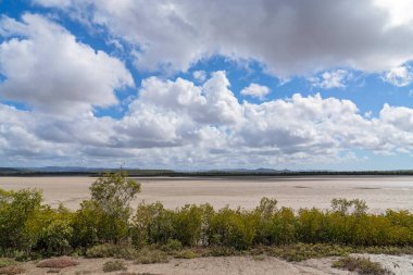 Kumlu bir dere yatağı, sular çekilmiş ve bulutlu mavi gökyüzünün altında hiç su yok.