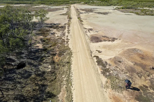 Aerial landscape of a dirt road with salt flats at low tide with drone operators under an umbrella. St Lawrence, Queensland, Australia