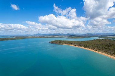 Mavi okyanusla çevrili uzun ve ıssız kumlu bir sahil ve yukarıda bulutlu bir gökyüzü, doğada güzellik. Johnsons Plajı, Sarina, Queensland, Avustralya