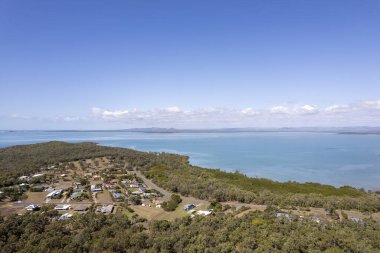 Mavi denizin kıyısındaki çalılıkların arasına kurulmuş küçük bir sahil kasabasının üzerindeki insansız hava aracı.