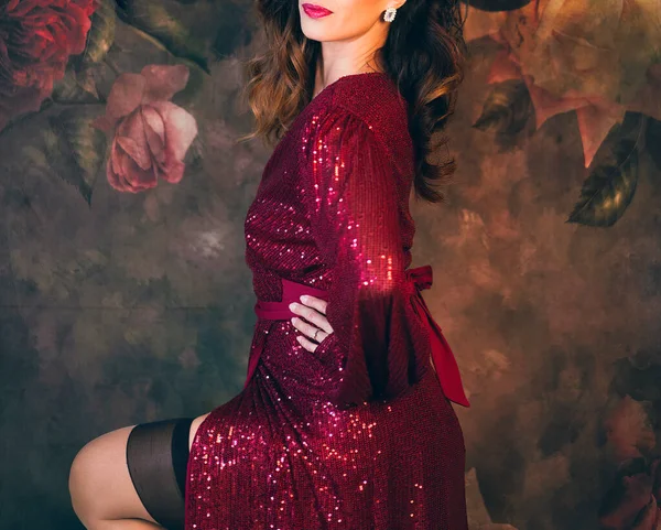 A burlesque dancer in a fancy costume posing for a photo shoot against a floral backdrop