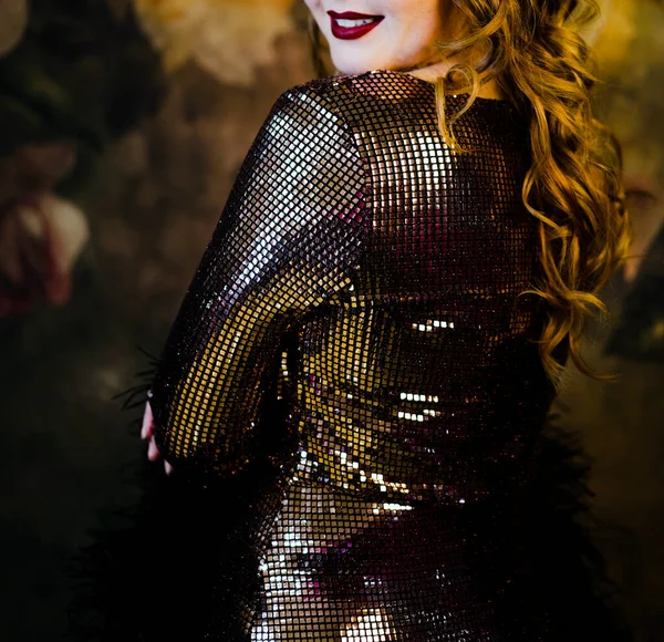 Glamorous burlesque dancer with long curly hair posing against a blurred backdrop