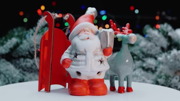 Juleleker av santa claus, et reinsdyr med slede, på bakgrunn av et juletre. – stockvideo