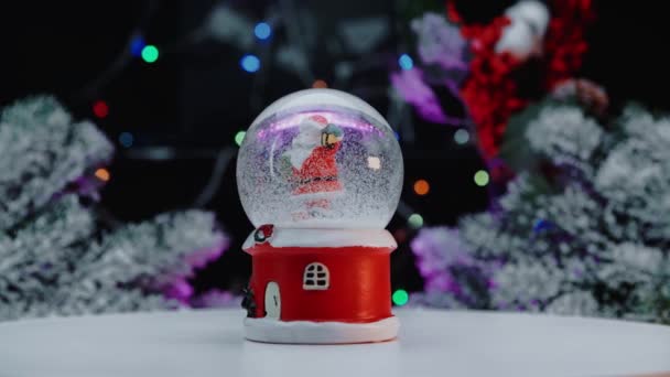 Palla di vetro di neve di Natale sullo sfondo di un albero di Natale con luci di Natale. — Video Stock