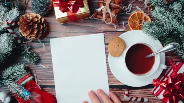 Decorations and hand putting a blank sheet of paper on the table stirring a mug with cocoa with a spoon. — Stock Video