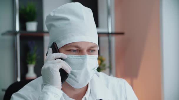 Um médico com uma máscara médica e uma máscara médica está falando ao telefone. — Vídeo de Stock