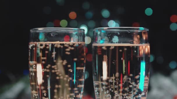 Primer plano de dos copas de champán sobre un fondo de luces de colores. — Vídeo de stock