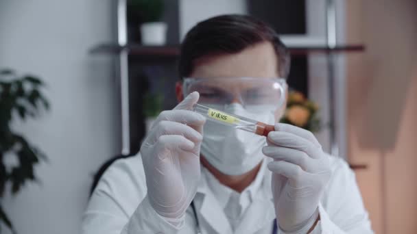 En laboratorieassistent undersöker ett provrör med ett farligt radioaktivt ämne märkt Virus. En man i skyddsmask och glasögon undersöker ett provrör. — Stockvideo