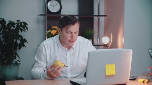 Bir adam işyerinde armut yer ve bilgisayarın önünde çalışır. Bir iş adamı bilgisayarın önünde ve ofis masasında yemek yer.. — Stok video