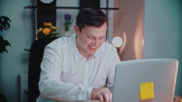 En voksen mand sidder på en bærbar computer. Han sms 'er og griner. – Stock-video