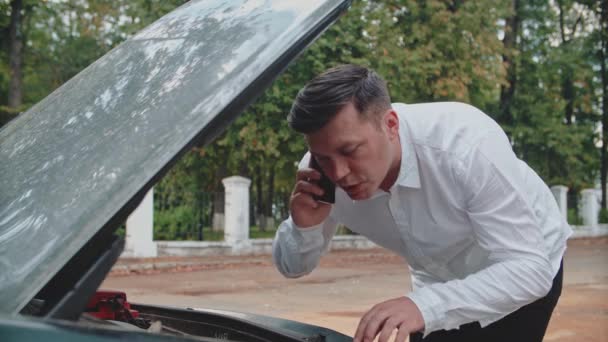 Araba bozuldu, bir adam telefonla konuşurken arabanın arızasını düzeltmeye çalışıyor.. — Stok video