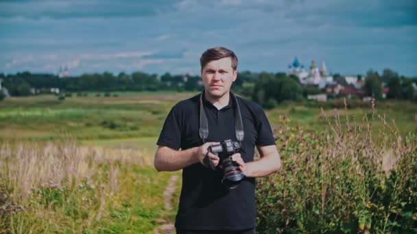 Portret van een reisfotograaf tegen de achtergrond van een landschap, klooster. — Stockvideo