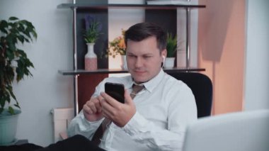 Masadaki bir adam akıllı telefon kullanarak kulaklıkla müzik dinliyor. Erkek işadamı dinleniyor..