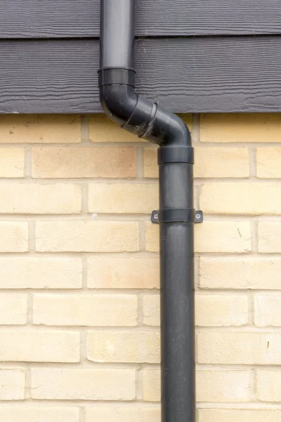 Close up of a black drainage pipe and clip on a brick wall — Stock Photo, Image