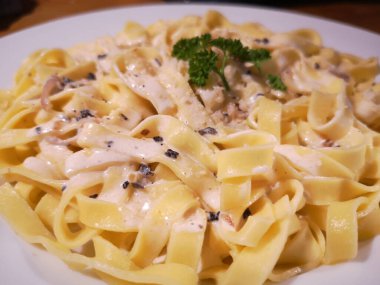 Yer mantarı soslu Tagliatelle, yuvarlak beyaz tabakta maydanozlu.