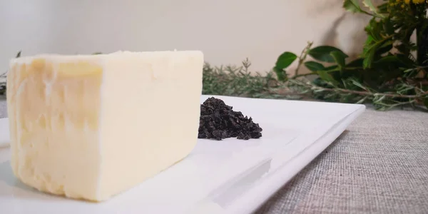 Beyaz dikdörtgen bir tabakta tereyağı ve kırık trüf mantarı arkaplanda Provence otları olan keten bir masa örtüsü.