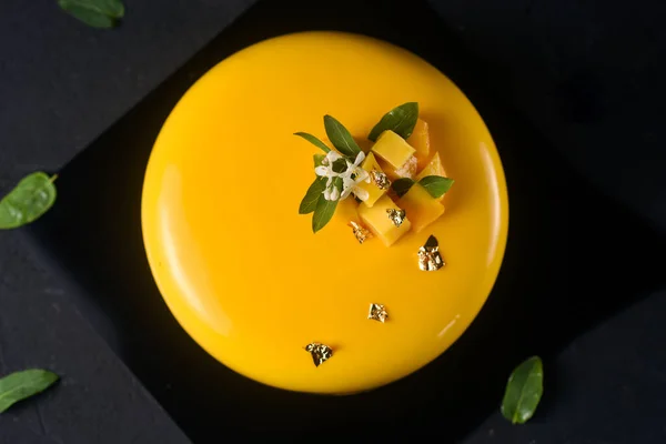 top view of yellow sponge cake with mango filling and the taste of a round-shaped ice cream on a refined black background.Delicate dessert combines juicy tropical aromas of mango and passion fruit