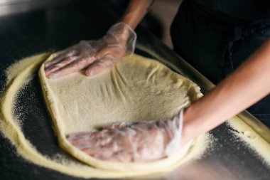 Demir mutfak masasında hamur mayasının bulanık görüntüsü. Eldiven giymiş bir aşçının elleri ve siyah önlük..