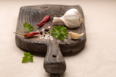 Farklı baharatlı klasik ahşap kesme tahtası: taze maydanoz yaprakları, kurutulmuş kırmızı acı biber, taze sarımsak, pembe deniz tuzu ve biber. Yiyecek arka planda..