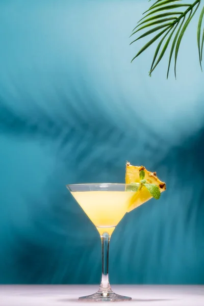 Cocktail rinfrescante all'ananas con fetta di ananas e menta davanti all'ombra delle foglie di palma in un sole splendente. — Foto Stock