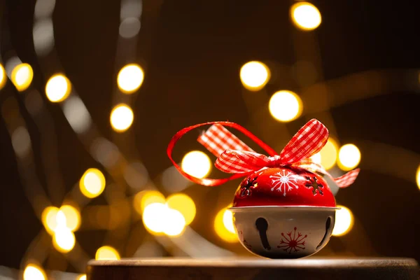 Świąteczna lub noworoczna kartka z dzwonkiem na modnym drewnianym podium przed świątecznymi lampkami w formie świątecznego bokeh.Close up. — Zdjęcie stockowe