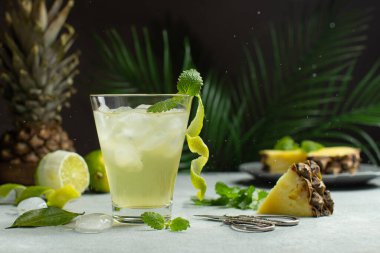 Ferahlatıcı, tropik ananas kokteyli ya da buzlu bir bardaktaki detoks suyu, palmiye yaprakları önünde nane ve limon. Ananas kokteyline yakın..