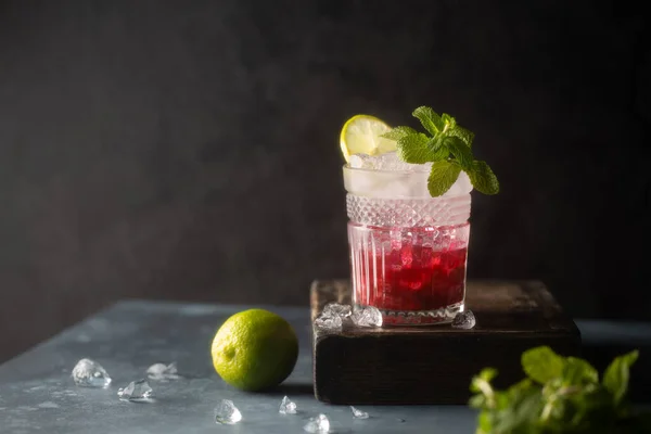 Refreshing cocktail with berry syrup or liqueur,tonic,crushed ice,fresh mint and lime on dark background.Copy space.