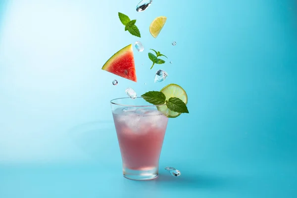 Cocktail all'anguria con cubetti di ghiaccio, vite di menta e lime su fondo azzurro.Colpo di bevanda in freeze motion, ghiaccio volante, foglie di menta e anguria.. — Foto Stock