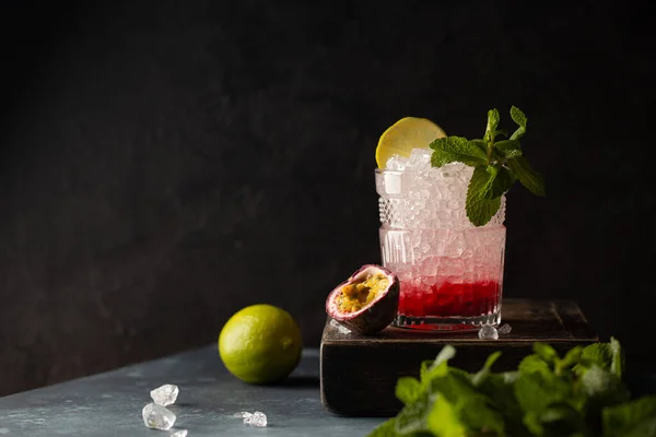 Cocktail rinfrescante con vodka, soda, purea di frutti di bosco, lime, menta, frutto della passione e ghiaccio tritato in vetro cristallo pregiato su scatola di legno e fondo scuro.. — Foto Stock