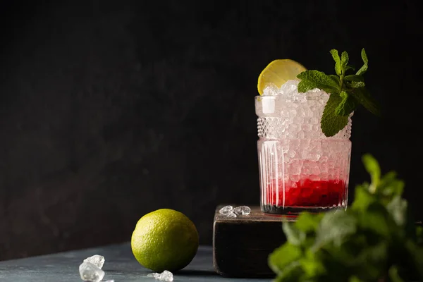 Cocktail rinfrescante con vodka, soda, purea di frutti di bosco, lime, menta e ghiaccio tritato su scatola di legno e fondo scuro. — Foto Stock