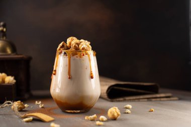 Sweet Milkshake with caramel syrup,cream liqueur,caramel popcorn and chocolate powder on brown background with vintage,manual coffee grinder. clipart